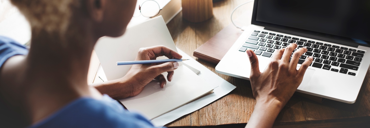 person using a laptop and ready to take notes with a pen on paper